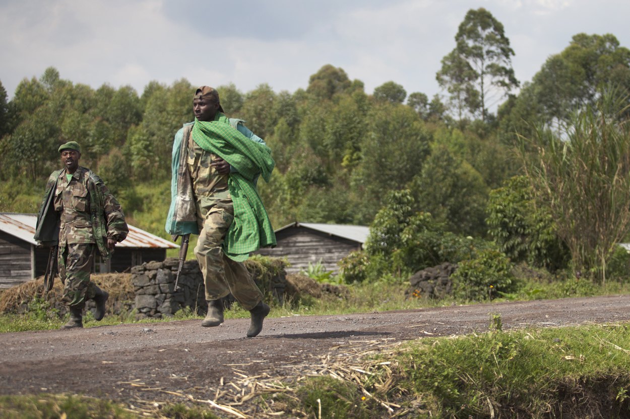 M23 fighters walking along a dirt road towards Goma, eastern Congo, with green hills behind