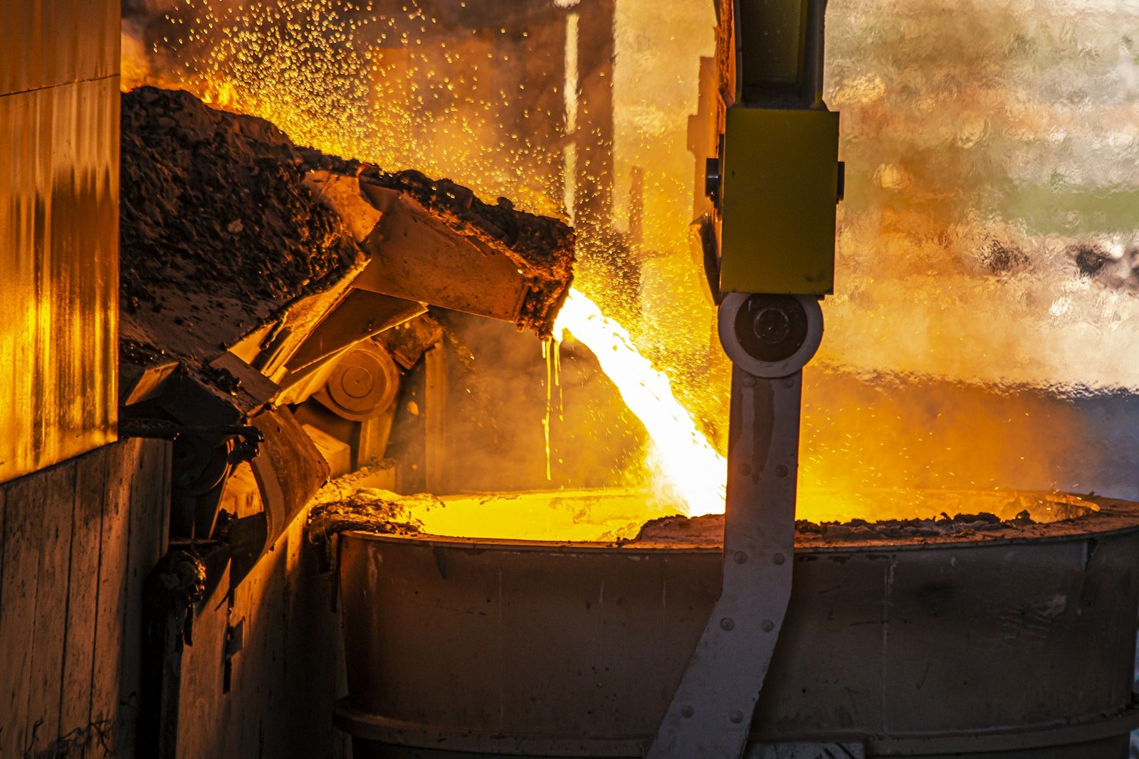 Molten metal pouring in a bright golden stream from a furnace into a steel ladle amid sparks