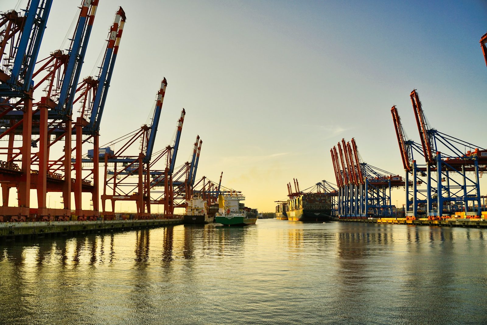 Container port cranes and departing cargo ship in warm golden dawn light