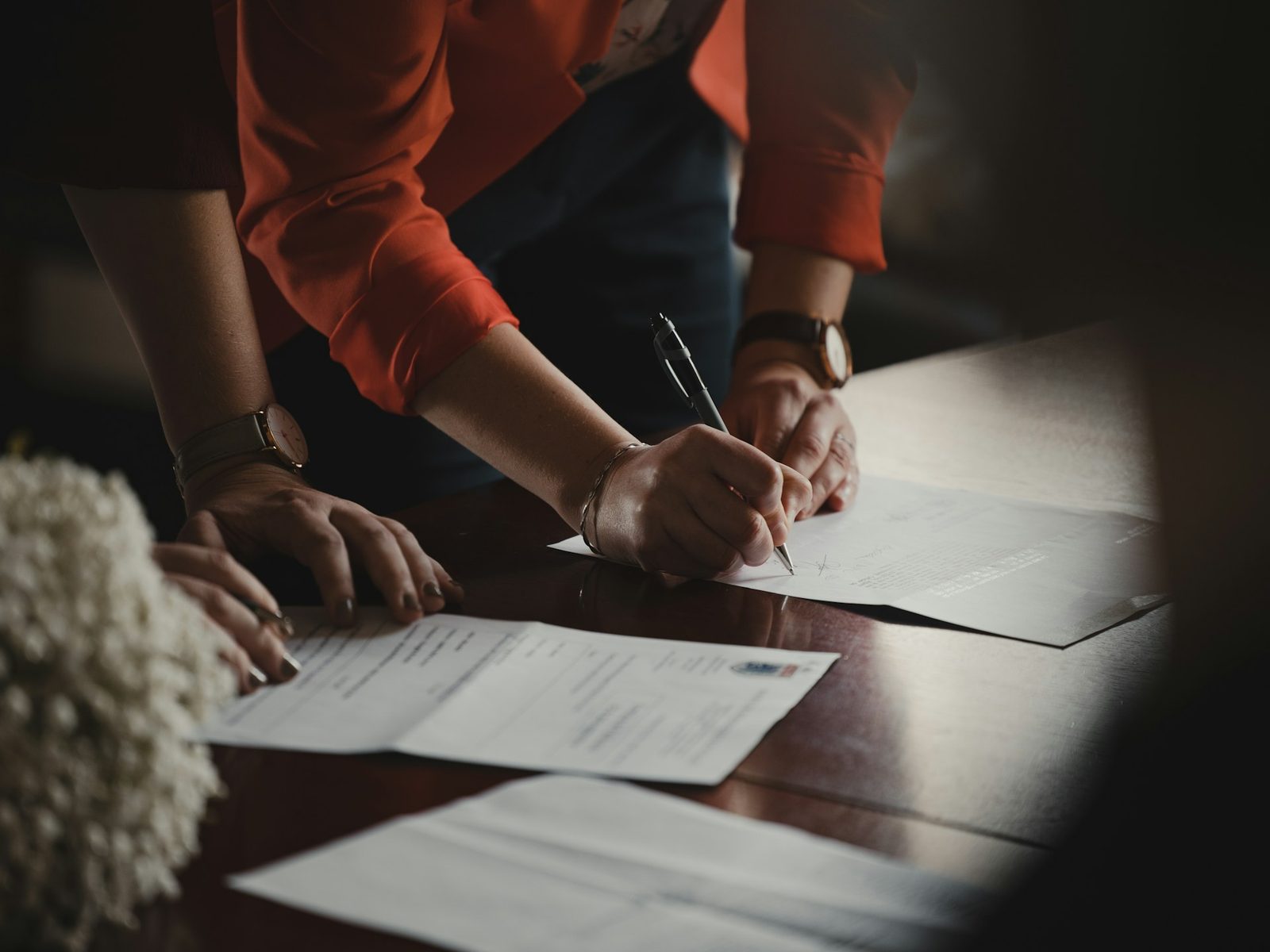 Two people signing agreements at a dark table