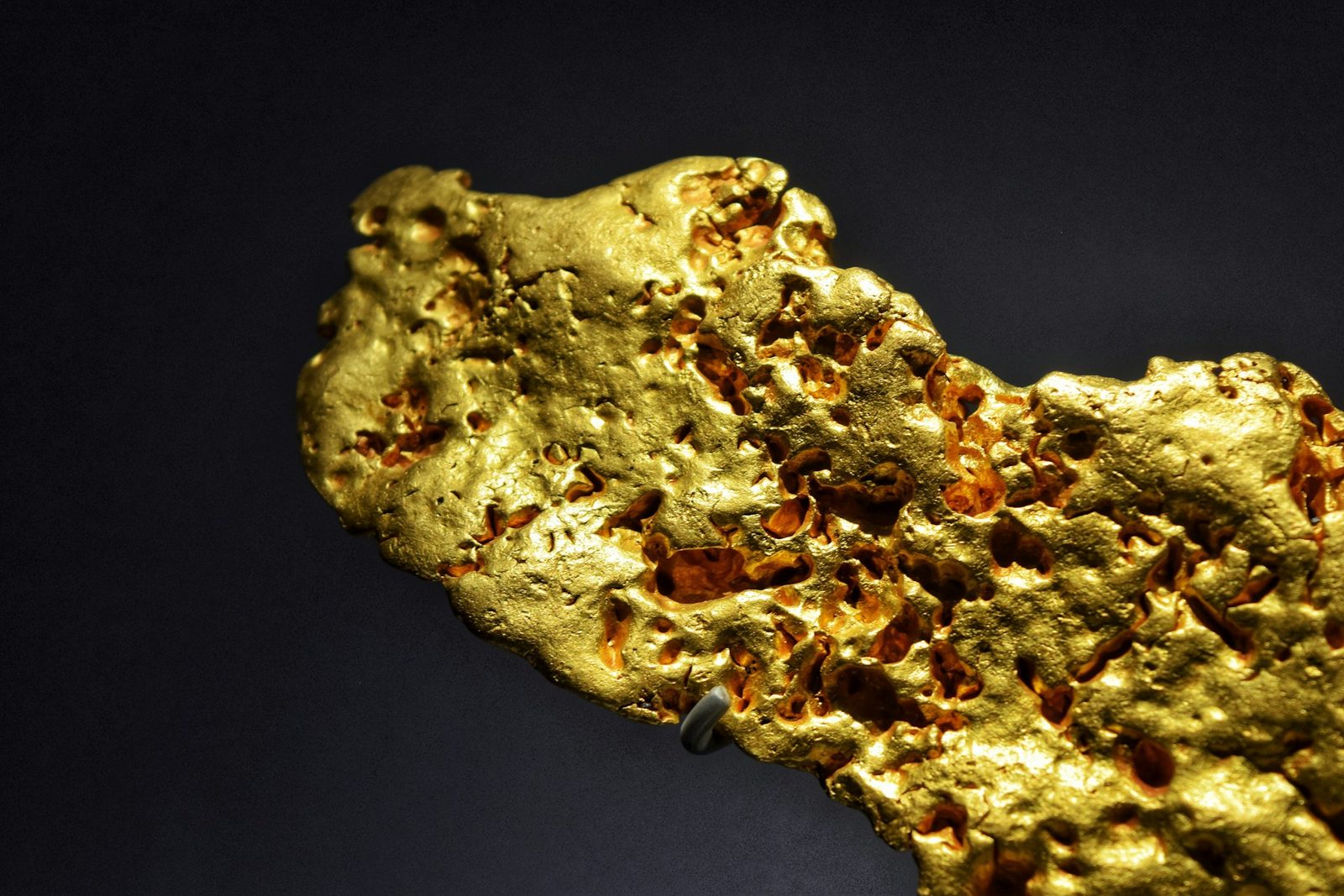 Large natural gold nugget with pitted surface against a dark navy background