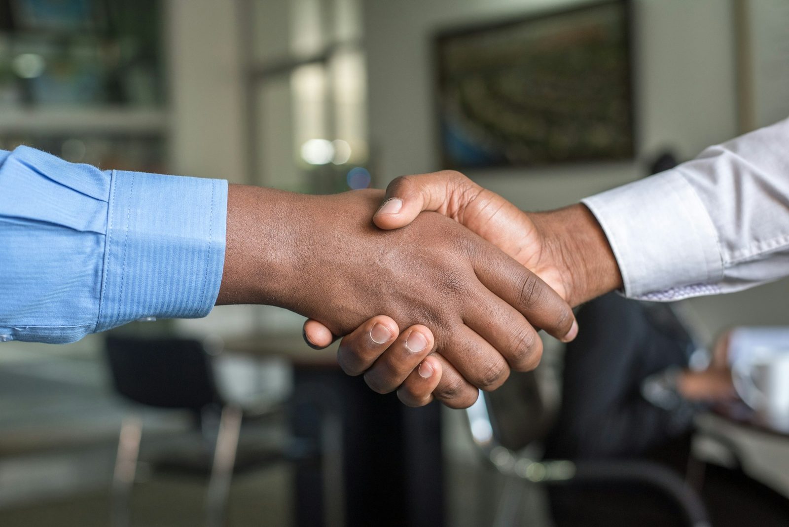 Two African professionals shaking hands across an office table, sealing a partnership.