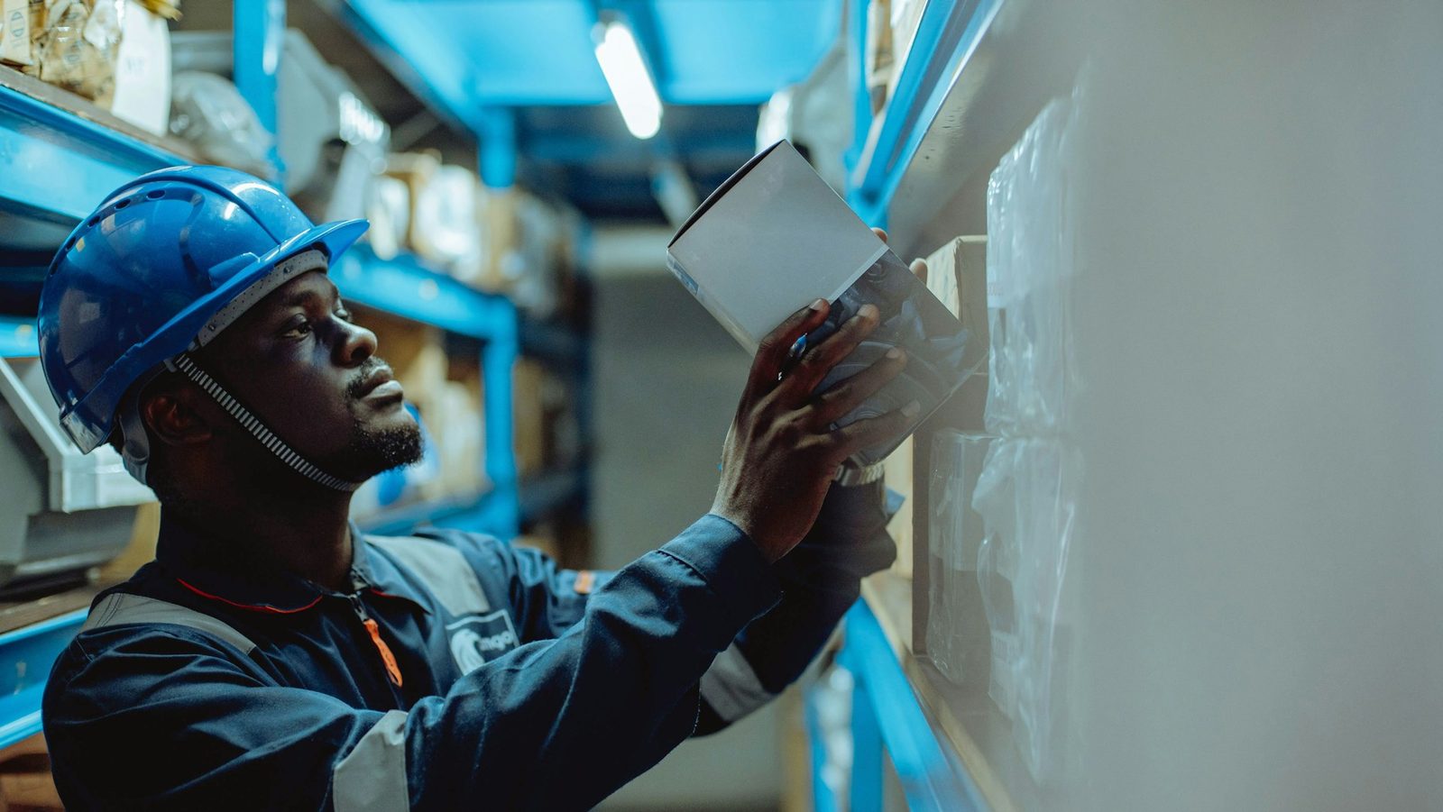 Warehouse technician in blue hard hat records inventory on steel racking