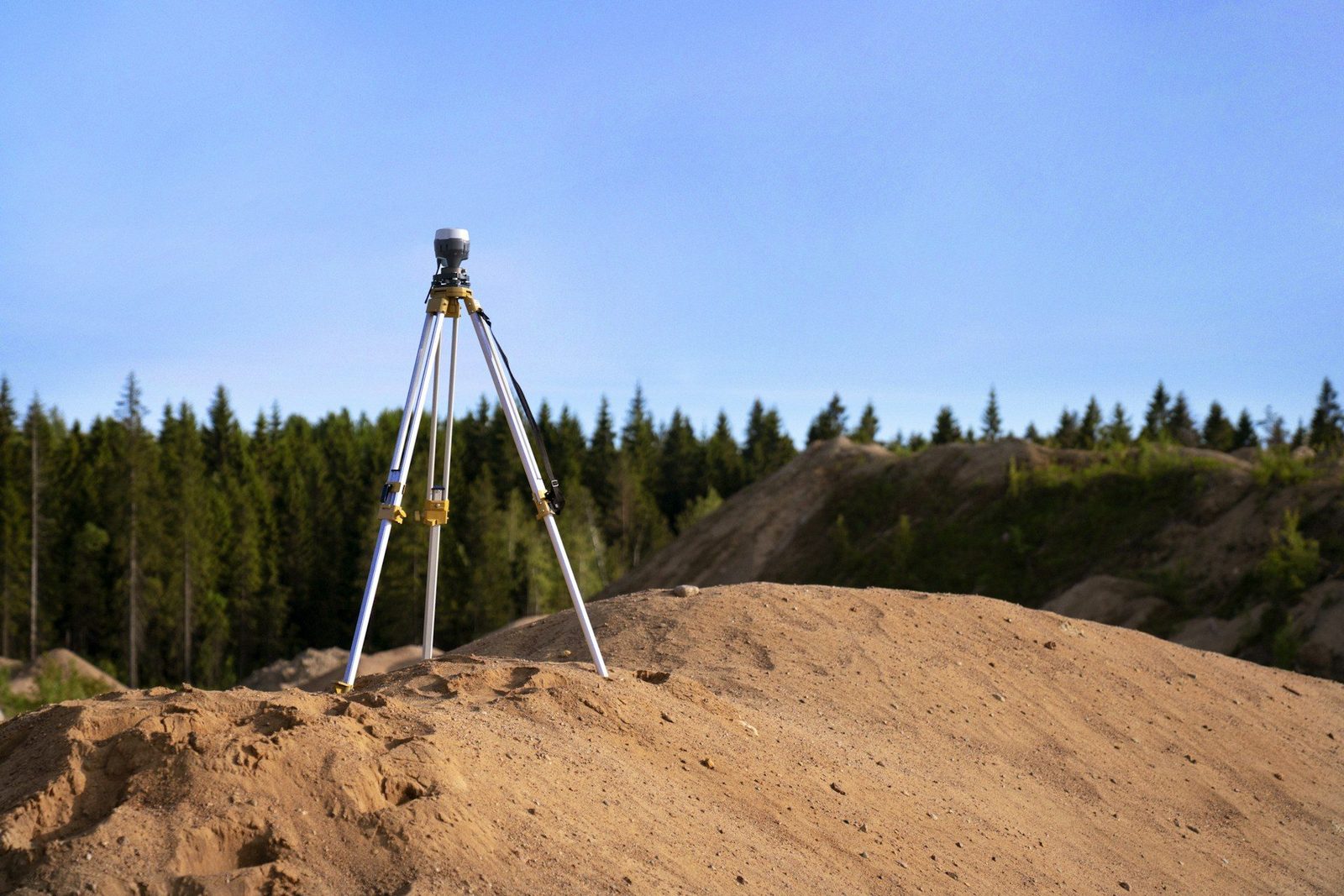 Survey receiver on a tripod standing on a mound of raw earth at a quarry under a blue sky